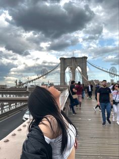 a woman looking up at the sky while standing on a bridge with people walking across it