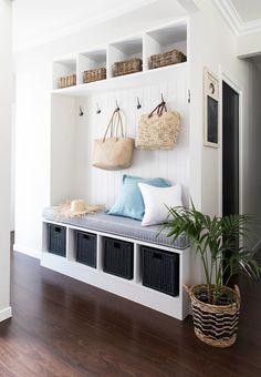 a white bench with baskets on it and two plants in the corner next to it