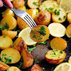 someone is holding a fork over some potatoes with lemons and parsley on top