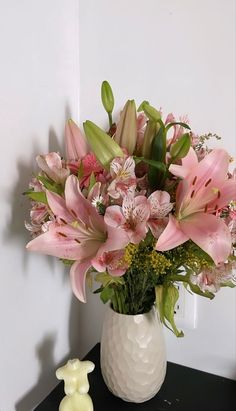 a white vase filled with pink flowers on top of a table next to a teddy bear