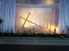 a window with curtains and flowers in front of it that has a crucifix on top