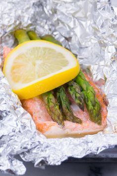 a piece of fish with asparagus and lemon on it sitting on aluminum foil