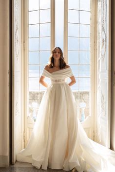 a woman standing in front of a window wearing a white dress