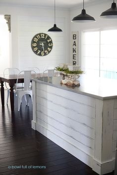 a kitchen with white walls and wood flooring next to a clock on the wall