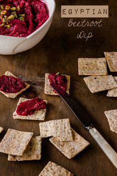 crackers with beetroot dip on them next to a bowl of fruit and a knife