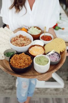 a woman is holding a tray with many different foods in bowls and sauces on it