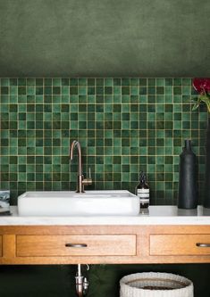 a bathroom with green tiled walls and wooden cabinets, sink and vases on the counter