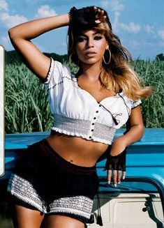 a woman in short shorts and crop top posing next to a white car with her hands on her head