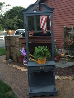 a blue grandfather clock sitting on top of a brick walkway next to a garden area