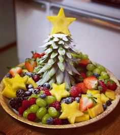 a wooden plate topped with fruit and a christmas tree made out of pineapples