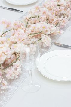 the table is set with white plates, silverware and pink flowers