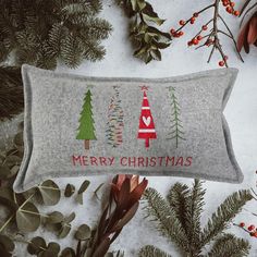 a grey pillow with christmas trees on it next to evergreen branches and red berry berries