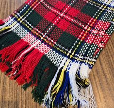 a red, white and black plaid blanket laying on top of a wooden floor with fringes