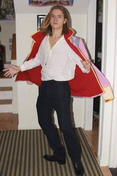 a woman standing in a hallway with a red cape on her shoulders and black pants