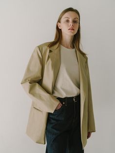 The individual is wearing an oversized blazer with a notched lapel, a contemporary take on classic suiting. The blazer has a single-button closure, which creates a streamlined and modern look. Its length extends to mid-thigh, offering a relaxed and stylish silhouette that could easily transition from office wear to casual settings. The fabric seems to have a smooth texture and a slight sheen, suggesting a blend that may include materials like viscose or silk.- The oversized fit is a nod to current trends, providing a comfortable yet chic aesthetic.- The neutral tone of the blazer makes it a versatile piece for layering over different outfits.- The simplicity of the design, with minimal visible detailing, gives this blazer a clean and sophisticated finish. Classic Everyday Blazer With Lapel Collar, Classic Blazer With Lapel Collar For Everyday, Classic Everyday Blazer With Hidden Button Closure, Classic Tailored Everyday Blazer, Classic Tailored Blazer For Everyday Wear, Tailored Blazer With Lapel Collar For Everyday, Classic Everyday Blazer For Spring, Classic Everyday Spring Blazer, Elegant Everyday Blazer With Notch Lapel