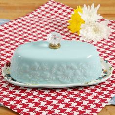 a blue cake sitting on top of a red and white checkered cloth next to flowers