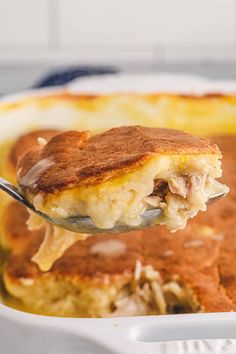 a spoon full of food is being lifted from a casserole dish with meat and cheese