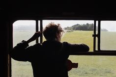 a person standing in front of a window looking out at an open field and trees