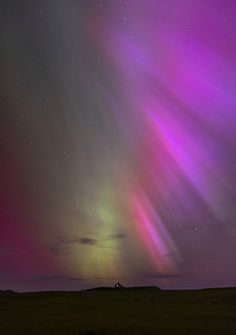 an aurora bore is seen in the night sky over a field with grass and trees