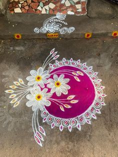 a pink and white flower design on the ground next to some rocks with flowers painted on it