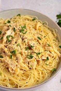 a white bowl filled with pasta covered in sauce and parsley on top of a table