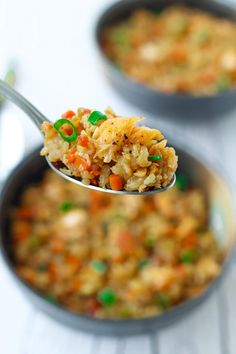 a spoon full of fried rice with carrots and green onions on it, in a bowl