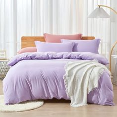 a bed with purple sheets and pillows in a room next to a white rug on the floor