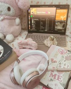 an open laptop computer sitting on top of a bed next to headphones and books