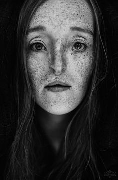 a black and white photo of a woman with freckles on her face, looking at the camera