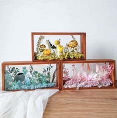 three wooden frames with flowers and plants in them sitting on a wood floor next to a white wall