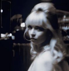 a blurry photo of a woman with long blonde hair in a white dress looking at the camera