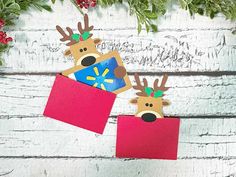 two paper reindeers with christmas decorations on their heads are hanging from the side of a white wooden wall