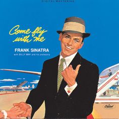 a man in a suit and hat standing next to another man on the beach with an airplane behind him