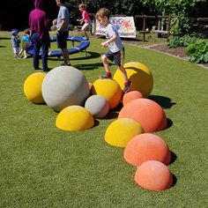 a young boy standing on top of colorful balls in the grass