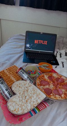 a laptop computer sitting on top of a bed next to two pizzas and waffles