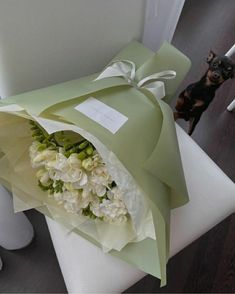 a bouquet of white flowers wrapped in green paper on a chair with a dog standing behind it