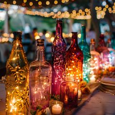 many different colored bottles are on the table with candles and lights in the back ground