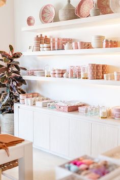 a room filled with lots of pink and white plates on shelves next to a potted plant