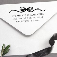 a white envelope with a black ribbon and address stamp on it, next to a plant