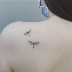 the back of a woman's shoulder with two small dragonflies on it