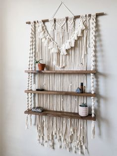 a macrame wall hanging on a white wall next to shelves with potted plants