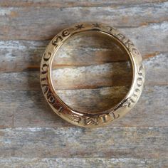 a close up of a ring with writing on it sitting on a wooden surface in front of a piece of wood