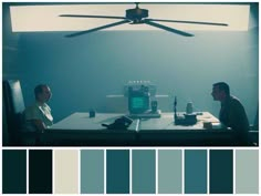 two men sitting at a table in front of a ceiling fan and color swatches