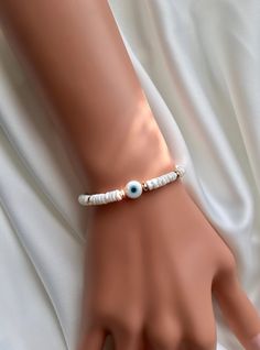 "These evil eye bracelets are handmade-to-order just for you! 🧿 Evil eye jewelry dates as far back as 3000 BC. Many ancient cultures wore amulets or jewelry with the evil eye symbol to protect them. Today the evil eye brings good luck and good vibes. An evil eye in white also represents purity, new beginnings, and wealth! Each one is made-to-order with genuine shell beads, gold plated hematite beads, and features a 10mm handmade lampwork evil eye. Because the beads are handmade each one is unique and there may be slight variations in the size and shape.  🧿 Materials: Handmade Lampwork Evil Eye Bead Genuine Shell Beads Gold Plated Hematite Beads Stretch Neoprene Cord 🧿 Sizing: Please measure your wrist before ordering. From the drop-down menu choose a size 1/2 inch bigger than your wrist Handmade White Evil Eye Bracelet For Beach, Elegant White Evil Eye Bracelet, White Evil Eye Bracelet Gift, Handmade Adjustable White Evil Eye Bracelet, White Beaded Evil Eye Bracelet, White Evil Eye Bracelet, Beaded Evil Eye, White Evil Eye, Eye Bracelets