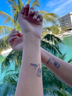 two people holding hands with tattoos on their arms and palm trees in the back ground