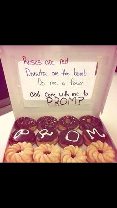 a box filled with lots of donuts sitting on top of a white table next to a sign