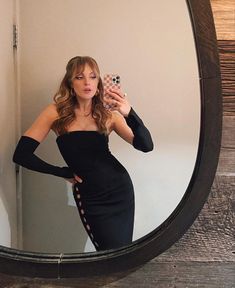 a woman in a black dress taking a selfie with her cell phone while standing in front of a mirror