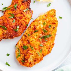 two pieces of fried chicken on a white plate with lemon wedges and parsley