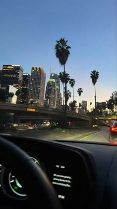 the view from inside a car looking at palm trees and city lights in the distance