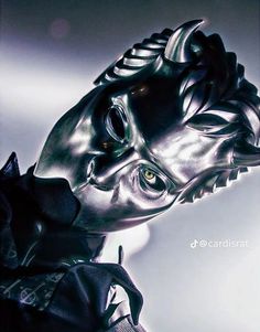 a close up of a metal mask on a white surface with light coming from behind it